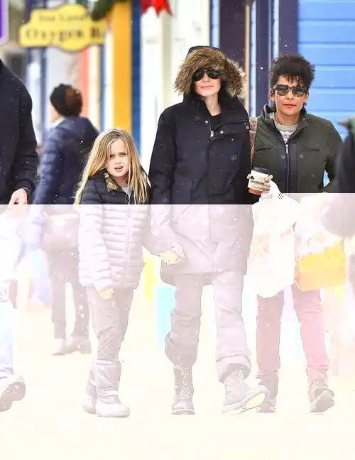  Huddling up: The young blonde, who looks strikingly alike to father Brad Pitt, kept cosy in a thick black puffer jacket and matching trousers and boots to her mother