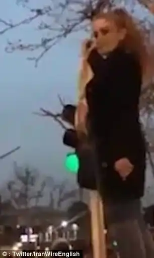 In the latest clip, the woman is seen raising the headscarf above her head by a set of traffic lights in Tehran