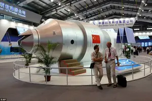 Visitors sit beside a model of China's Tiangong-1 space station in 2010. The station played host to two crewed missions and served as a test platform for perfecting docking procedures and other operations