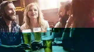 Four friends sitting at a pub table drinking a pint of beer.